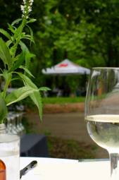 A glass of white wine on a white tablecloth with flowers at an outdoor party.