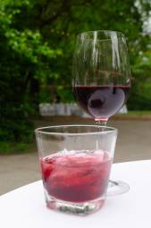 A red cocktail and a glass of red wine on a white table.