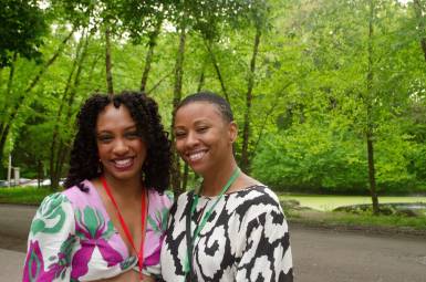 Two women in party clothes smile for the camera in an outdoor setting.