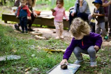 A child in a blue jacket crouches down to play while other children play in the background.