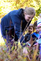 Four children and two teachers look at plants outdoors.