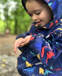 A young child in rain gear looks at a ladybug.