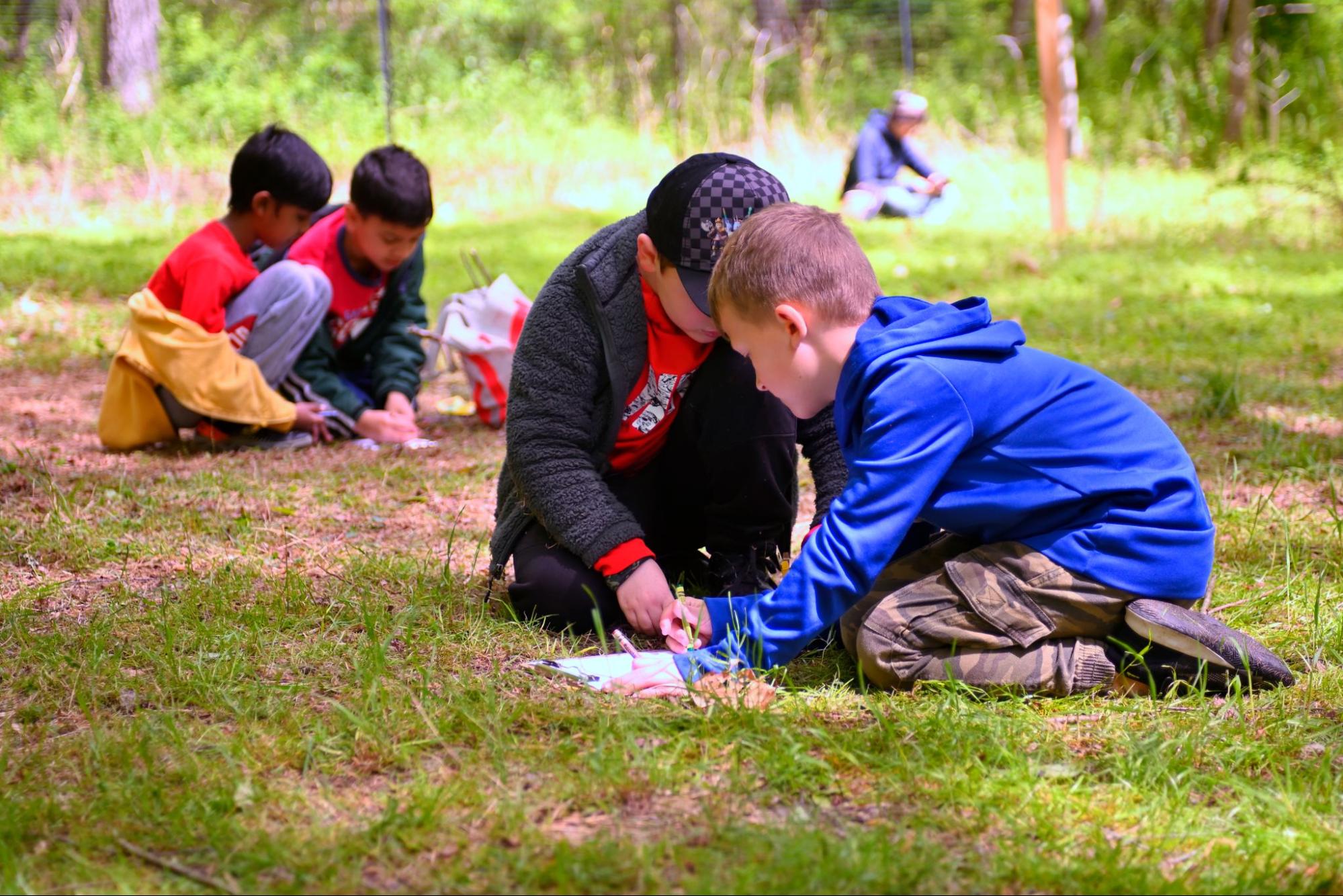 Five children kneeling on the ground drawing with crayons.