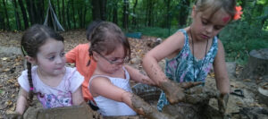 Four children play in a mud kitchen outdoors.