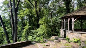 A stone and wood gazebo on the side of a stone amphitheater in a forest.