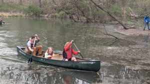 Two children and an educator paddle a canoe on a pond in the woods.