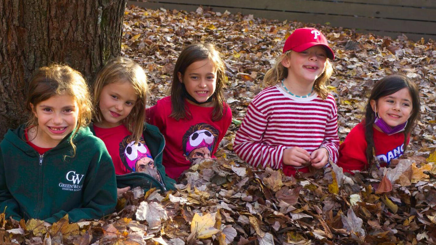 Five children sitting in a pile of autumn leaves. 