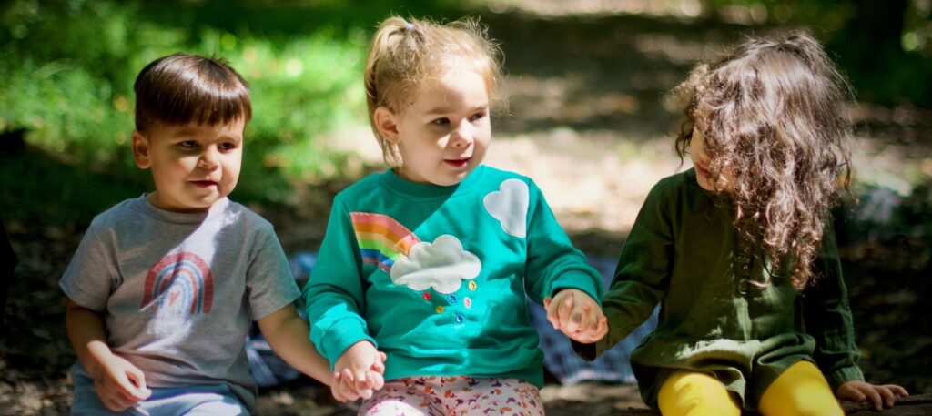 Three preschool age children sitting on a log outdoors.